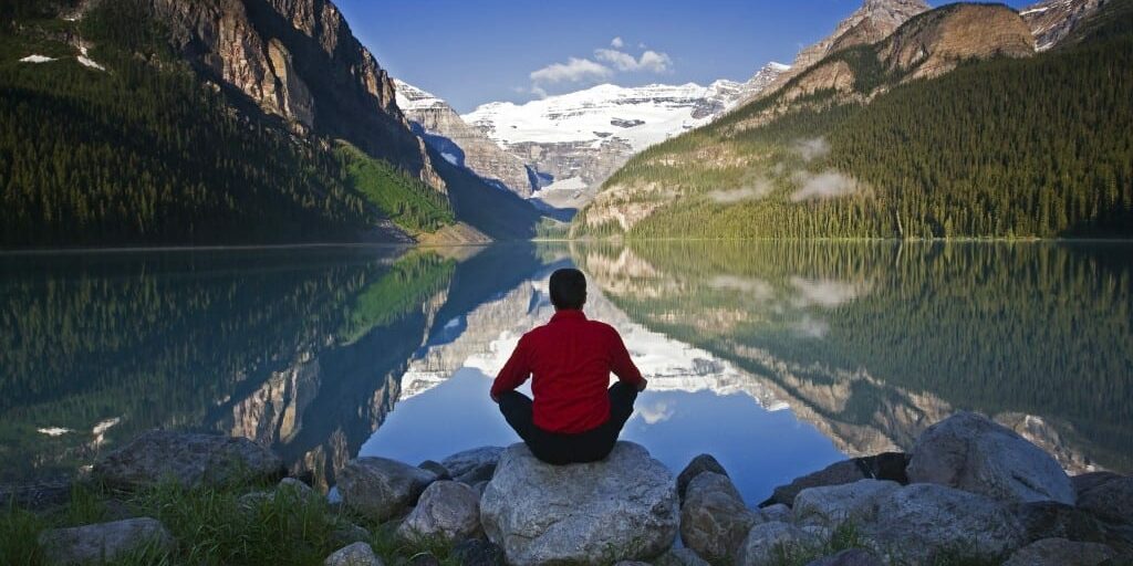 Middle age male meditating on rock at Lake Louise, Alberta, Canada.