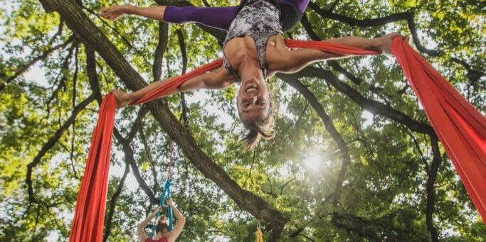 Aerial silk artist performing movements on ropes hanging from trees on a sunny day in Tivoli park, Ljubljana.