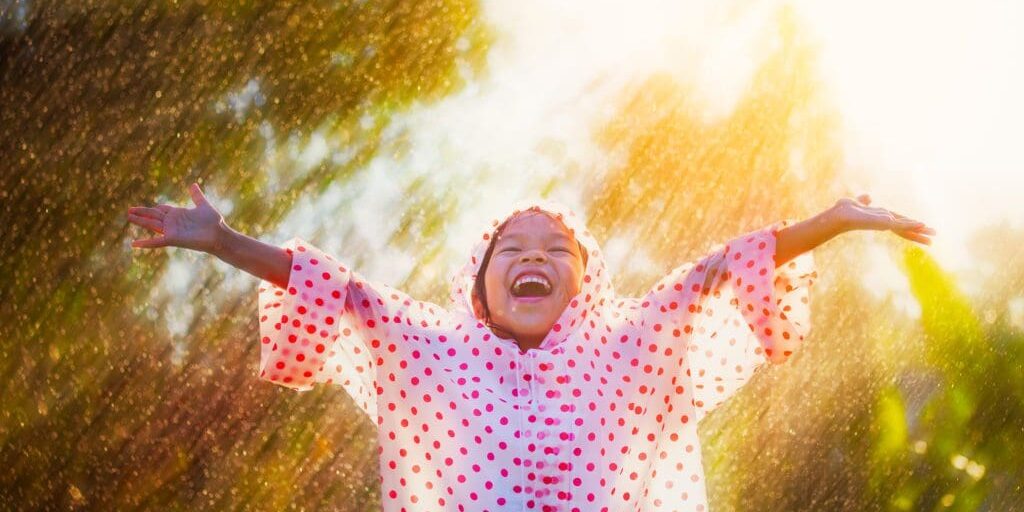 Happy asian child girl wearing raincoat having fun to play with the rain in the sunlight